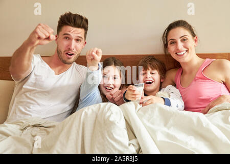 Famiglia e due bambini divertirsi guardando la tv nel letto in camera da letto Foto Stock