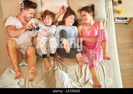 Famiglia con due bambini è felicemente scherzando intorno a letto in camera da letto Foto Stock