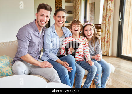 I genitori e i due bambini con un piccolo gatto sono seduti tranquillamente ridere in salotto Foto Stock