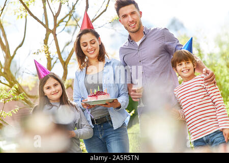 Famiglia con due bambini festeggiare il compleanno con la torta nel giardino in estate Foto Stock