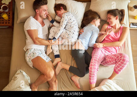 I bambini sono stupidi e giocare con i loro genitori felicemente in letto matrimoniale in camera da letto Foto Stock