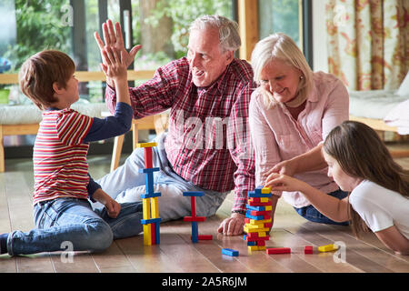 Il nonno e i nipoti si donano un alto cinque quando si gioca con la costruzione di blocchi a casa Foto Stock