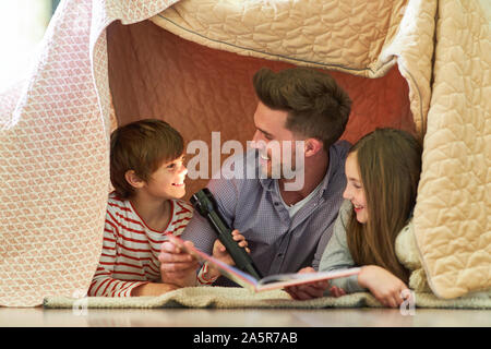 Padre con la torcia elettrica legge libro insieme con i bambini al di sotto di una coperta Foto Stock