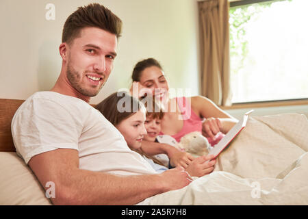 Felice famiglia con due bambini con libro durante la lettura insieme a letto Foto Stock