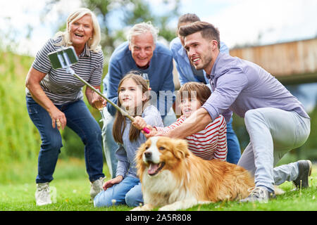 Famiglia estesa con i nonni e due bambini rende selfie con il cane in giardino Foto Stock