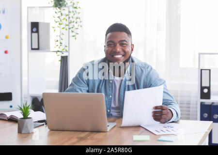 Allegro afro imprenditore lavora con il computer portatile e i documenti di office Foto Stock