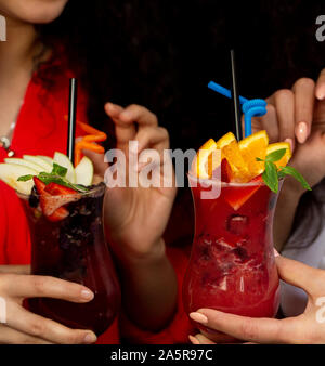 Due donna azienda bicchieri di cocktail di frutta con arancia, fragola e apple, fragola Foto Stock