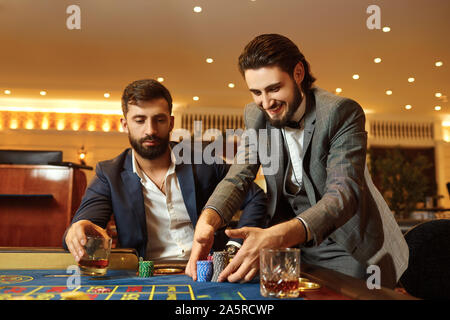 Uomo di gruppo in un vestito al tavolo della roulette giocando a poker in un casinò. Foto Stock