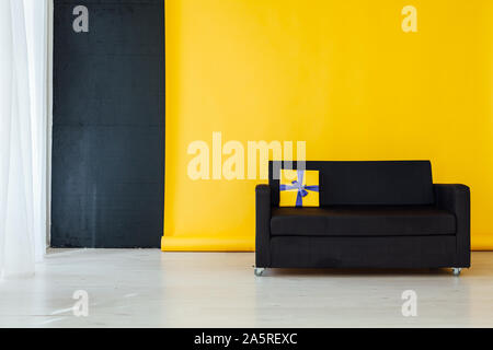 Divano nero con doni all'interno della camera con uno sfondo giallo Foto Stock