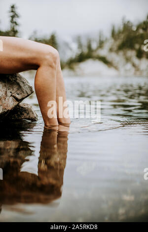 Una chiusura delle gambe femmina con i piedi immersi in un lago alpino. Foto Stock