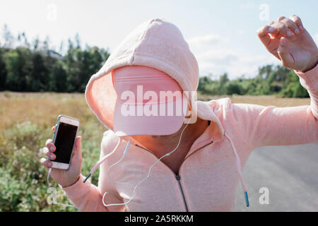 Donna che mantiene il suo telefono e cuffie ballando al di fuori del paese Foto Stock