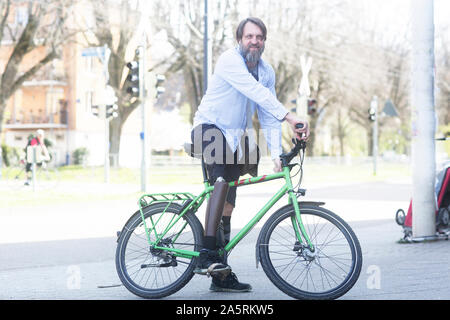 Uomo vecchio con gamba protesico tornando a casa con una bicicletta Foto Stock