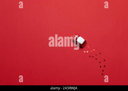 Vista superiore lucida piccolo giocattolo auto con golden star brilla su di uno sfondo di colore rosso. Messaggio di saluto festivo card o banner. Foto Stock