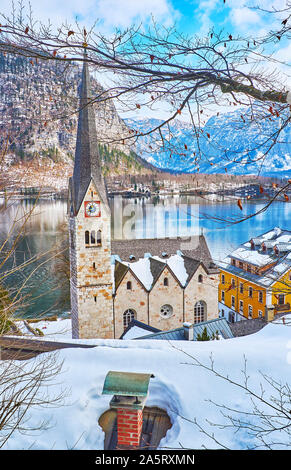 Città vecchia a piedi con una vista sulla chiesa evangelica edificio, visto attraverso i rami di alberi e neve tetti di Halltatt, Salzkammergut, Austria Foto Stock