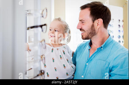 La cura della salute, la vista e il concetto di visione. Bambina scelta di occhiali con padre al negozio di ottica Foto Stock