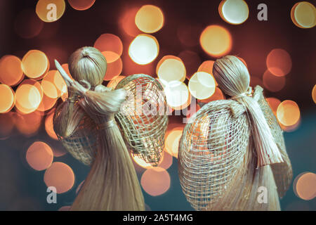 Paglia di due angeli in preghiera su una sfocata sullo sfondo di Natale. Bellissimo bokeh creato da luci di Natale. Tradizionali fatti a mano la bambola come un regalo di Natale tre Foto Stock