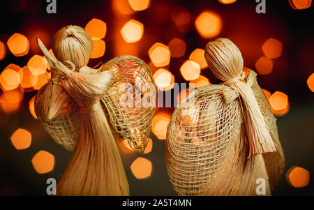 Paglia di due angeli in preghiera su una sfocata sullo sfondo di Natale. Bellissimo bokeh creato da luci di Natale. Tradizionali fatti a mano la bambola come un regalo di Natale tre Foto Stock