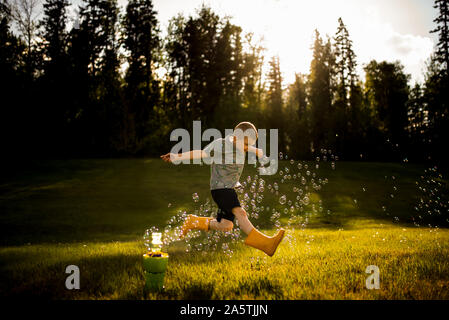 5 anno vecchio ragazzo saltando attraverso le bolle nella luce dorata Foto Stock