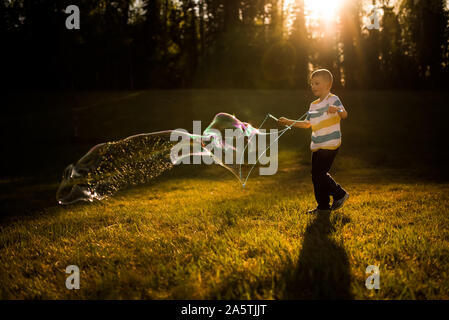5 anno vecchio ragazzo rendendo bolla gigante a ora d'oro Foto Stock
