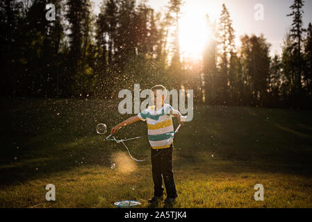 5 anno vecchio ragazzo bolla gigante pop nella luce dorata Foto Stock