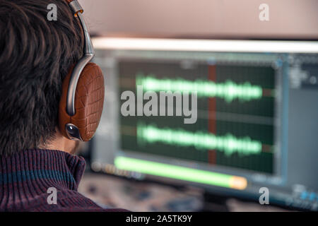 L'uomo della foto in studio i record e modifica il canto, voce e musica per uso commerciale. Lavora in un editor audio in un computer con cuffie Foto Stock