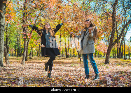 Due amiche ingannare intorno con foglie di giallo a City Park Foto Stock