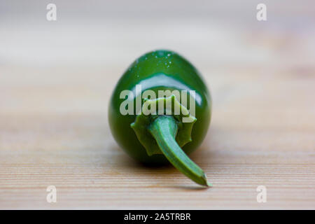 Vicino la foto di un jalapeño Peperoncino (Capsicum annuum) su una superficie di legno. Il peperoncino jalapeno è verde e lucente. Lo sfondo è sfocato e luminose Foto Stock