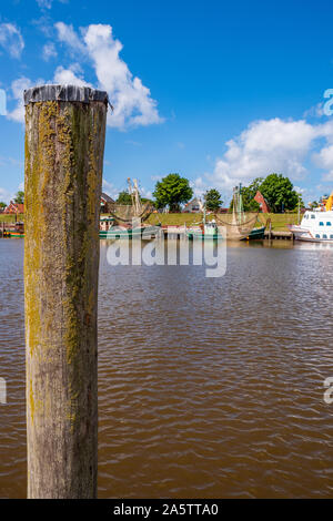 Palo di legno nella metà sinistra della foto, trawler e granchio le barche nel porto di Greetsiel fuori fuoco in background, Bassa Sassonia, Germania Foto Stock