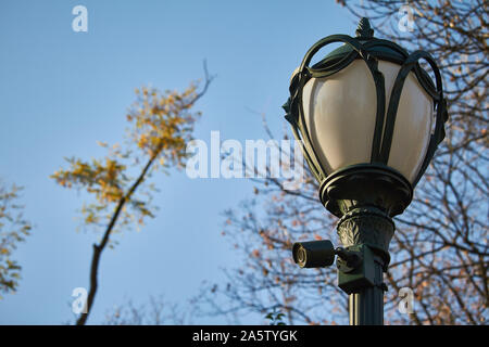 Lanterna Vintage con telecamera di sorveglianza in un parco pubblico in autunno davanti a un cielo blu, il fuoco selettivo Foto Stock