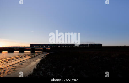 Silhouette di una DRS classe 37 locomotore trasporta un Arriva Nord del trasporto ferroviario di passeggeri in treno attraverso Eskmeals viadotto sulla la costa del Cumbria linea. Foto Stock