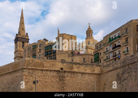 La Valletta mura di fortificazione e la città di edifici famosi shot dal porto dei traghetti. Torre della Cattedrale Anglicana di San Paolo e la parte superiore della chiesa carmelitana la cupola Foto Stock