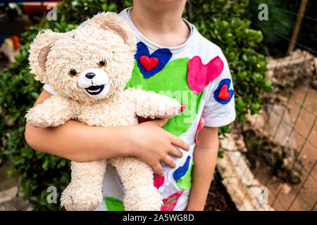 Strana scena del ragazzo con cuori t-shirt tenendo un sporche e vecchie Teddy bear. Foto Stock