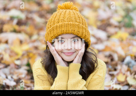 Caldo accessorio di lana. Ragazza capelli lunghi faccia felice la natura in autunno sfondo. Bella stagione. Mantenere caldi questo autunno. Il bambino nel cappello giallo all'esterno. In autunno la cura della pelle di routine. Kid indossare Caldo berretto lavorato a maglia. Foto Stock