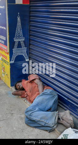 PONDICHERRY/India-febbraio 22 2018:senzatetto uomo dorme in modo irregolare a fronte di un negozio porta sulle strade di Pondicherry. Foto Stock