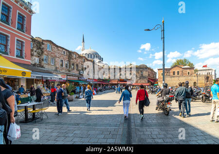 I turisti e i Turchi godono di una soleggiata giornata estiva tra i caffè sulla Piazza Eminonu con la Yeni nuova moschea in vista dietro. Foto Stock