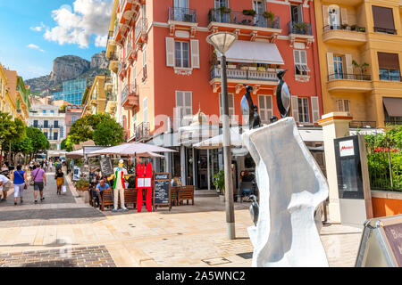 Turisti e il monegasco locali godono di una soleggiata giornata estiva dello shopping e la ristorazione in Monte Carlo, Monaco, con ripide montagne in distanza. Foto Stock