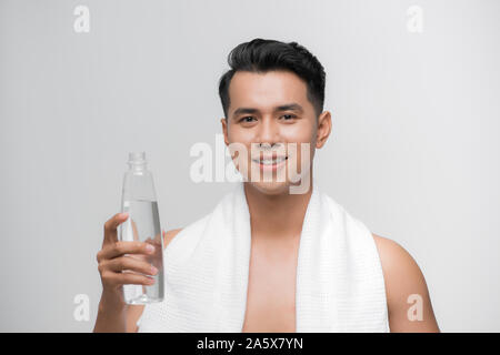 Immagine del bel uomo sorridente con asciugamano bianco sulle sue spalle tenendo la bottiglia di acqua dopo allenamento sfondo bianco Foto Stock