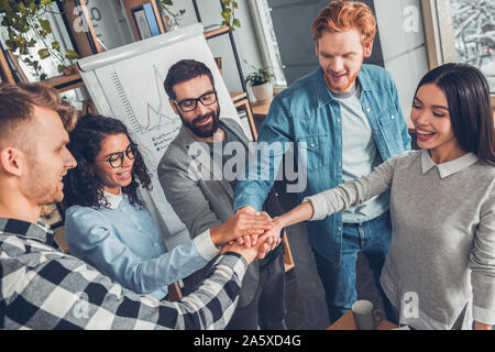 Startupers lavorando in ufficio insieme in piedi tenendo le mani vista dall'alto spirito di squadra Foto Stock