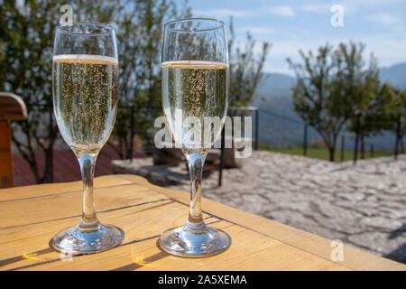 Due bicchieri di champagne contro uno sfondo sfocato di alberi e montagne. Foto Stock