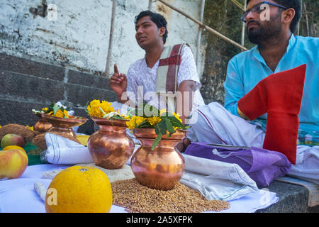 Un sacerdote Indù (l) al serbatoio Banganga, Walkeshwar, Mumbai, India, con offerte di fronte, la conduzione dei riti in onore di un uomo (r) defunto rispetto Foto Stock