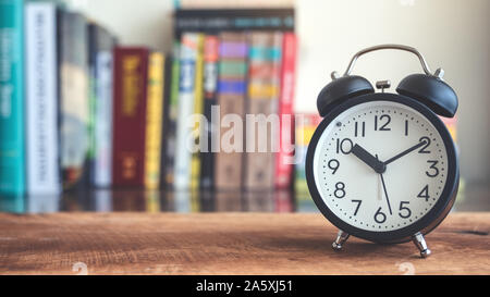 Primo piano immagine di un nero orologio sveglia sul tavolo di legno con scaffale di sfocatura sullo sfondo Foto Stock