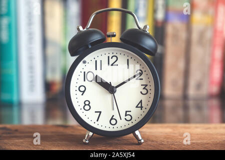 Primo piano immagine di un nero orologio sveglia sul tavolo di legno con scaffale di sfocatura sullo sfondo Foto Stock