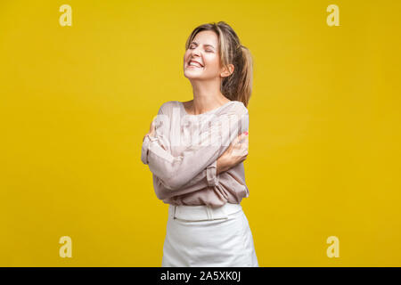 I love me. Ritratto di orgogliosa bella donna con capelli biondi nella camicia casual in piedi con gli occhi chiusi, abbracciando se stessa, il rispetto e la stima di sé Foto Stock