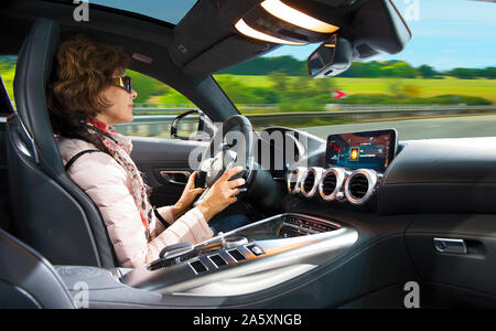 Donna adulta alla guida di una super auto moderna in autostrada. La guida è un piacere Foto Stock