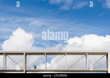 Due persone a piedi su una sospensione ponte pedonale con una drammatica sky in background nel distretto governativo di Berlino, Germania Foto Stock