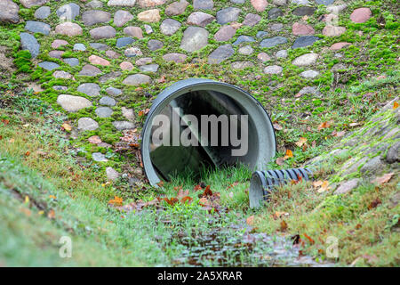 Tubo di drenaggio. Canale sotterraneo sotto la piccola strada. Fossa di scarico e le tubazioni in città Foto Stock