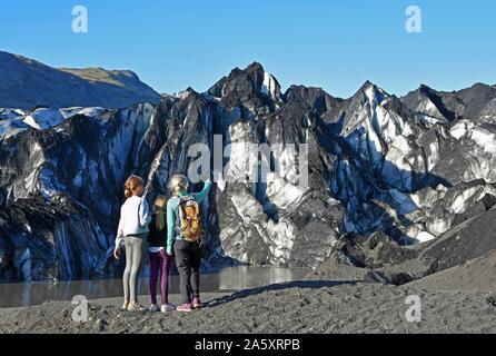 Madre di due figli guarda il ghiacciaio Solheimajokull, Solheimajokull, lingua del ghiacciaio di Myrdalsjokull compresi ceneri vulcaniche, vicino a corona Foto Stock