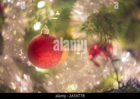 Close-up su un ramo di un albero di Natale decorato. Una lampadina rossa è la messa a fuoco e ci sono sfocati glitter e luci nella struttura ad albero . Foto Stock