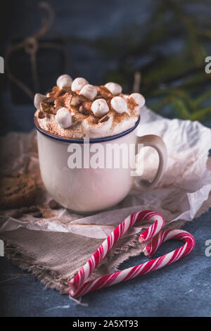 Lussuoso cioccolata calda con panna montata e pezzi di marshmallows e scaglie di cioccolato in una tazza di colore bianco su sfondo blu. Di fronte all'chocol Foto Stock