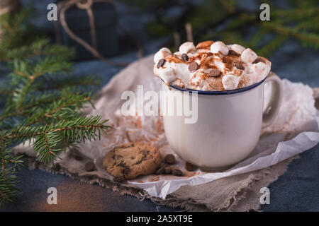 Lussuoso cioccolata calda con panna montata e pezzi di marshmallows e scaglie di cioccolato in una tazza di colore bianco su sfondo blu. Foto Stock